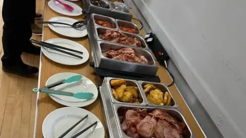 Contributed A picture of several containers that sit on a long table and are filled with various breakfast foods including bacon, hash browns and more. Plates with tongs rest in front of the containers.