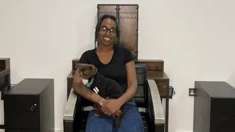 Ebuni Ajiduah A woman sat on a salon chair with a dog on her lap