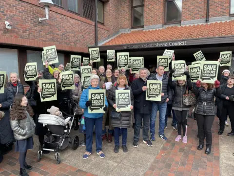 Local Democracy Reporting Service Protestors holding Save Leisure Gateshead placards stand outside the offices of Gateshead Council.