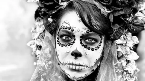 Terry Flaxton A photo of a woman dressed in a day of the dead costume, with white makeup and black eyes