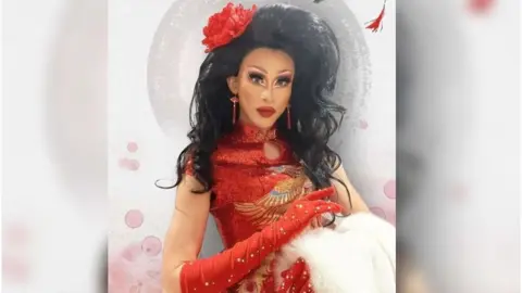 Zee A person in a red dress with a black wig and a flower in their hair