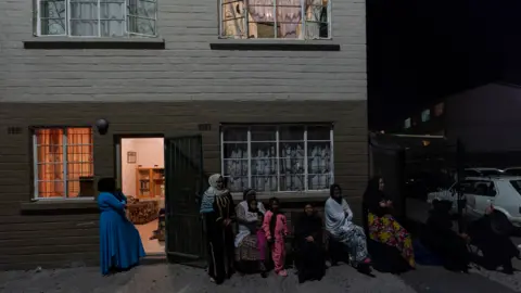 BBC/Shiraaz Mohamed People gathered outside their flats in Manenberg, Cape Town - South Africa