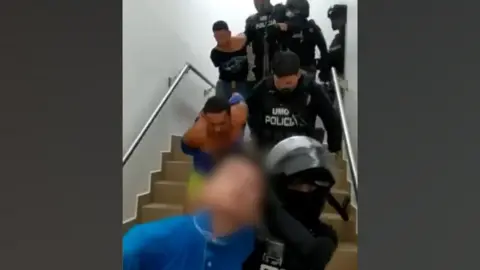 Policía Ecuador Police leading men out of a hospital after their arrest.