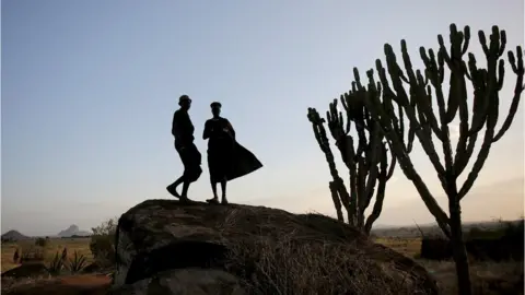 Reuters Two men standing on a rock. It is getting dark. You can just see their silhouettes.