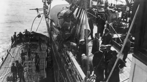 Getty Images Groups of men on the deck of a ship which laying telegraph cable at sea, with the image showing men looking over the side of the ship at a smaller vessel carrying the cable, circa 1900