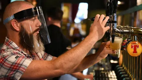 Reuters Man pours pint while wearing PPE visor