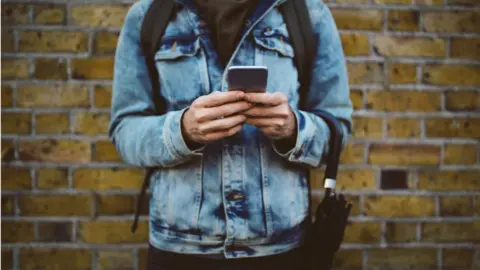 Getty Images Stock photo of a man in a demin jacket lookig at his phone