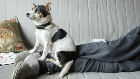 Margaret Mitchell Lily sitting on Max's legs whilst he is lying on the couch
