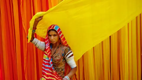 Getty Images India, Rajasthan, Sari Factory, Lesmay, 40 old. Textile are dried in the open air. Collecting of dry textile are folded by women and children.
