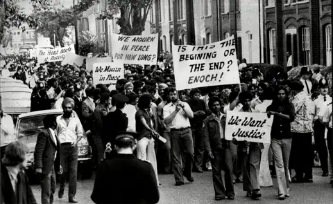 Bill Cross/ANL/Shutterstock Black & white still of protests, with a crowd of people marching and holding signs.