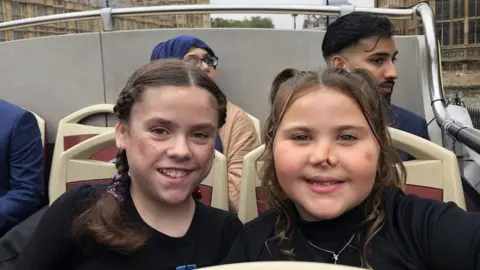 BBC Carmela and Harmonie-Rose both smile to the camera on an open-top bus tour