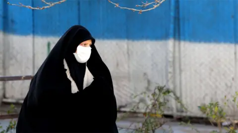 AFP A woman wearing a face mask walks down a street in Tehran (2 March 2020)