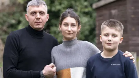 PA Media Ukrainian refugees Pavlo Romaniukha (left) with his wife Rymma Parkhomenko-Romaniukha and their son who fled Ukraine,