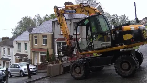 Digger moves concrete blocks into place on Waun-wen Road in Mayhill, Swansea