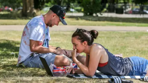 Getty Images A couple working on their laptops under the shade on a hot and sunny day London