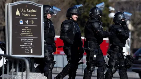 EPA/JUSTIN LANE US Capitol Police officers in riot gear walk through the grounds around the US Capitol on the day before the inauguration