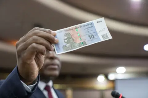 Getty Images Central Bank Governor John Mushayavanhu showing reporters the ZiG.