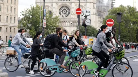 Reuters Bikers wearing protective masks ride past Notre Dame Cathedral