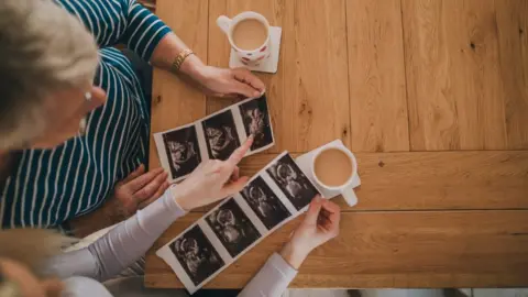 Getty Images Nan and niece viewing the new baby scan photos with a cup of tea in the dining room.