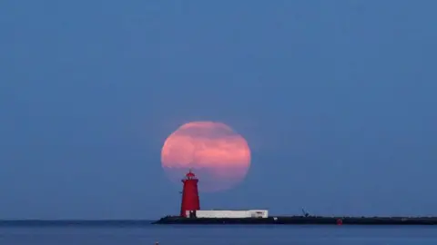 PA Media The final supermoon of the year rises over Poolbeg Lighthouse in Dublin Bay, Ireland