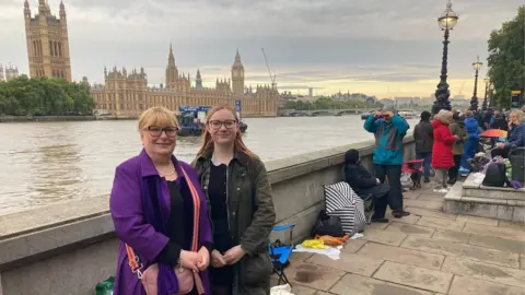 Justin Dealey/BBC Helen and Zara standing across the river from Houses of Parliament