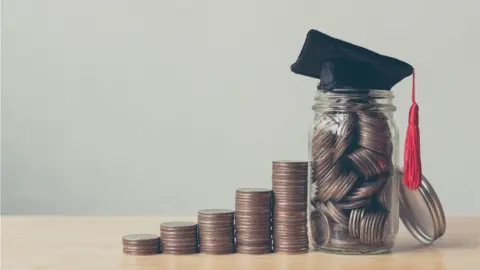 Getty Images Different sized piles of coins in a row, next to a jar with a mortar board on it