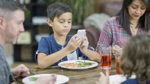 Getty Images A boy on his phone at the dinner table