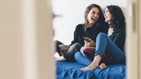 Getty Images Young people laughing sitting on a bed