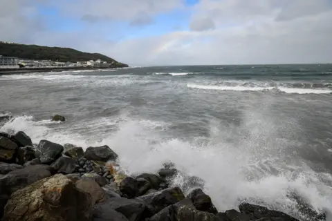 PA Media Rainbow above stormy sea