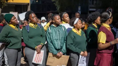 AFP School children lines up in a protest. They are wearing green school uniforms and looking to their left.