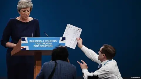 Getty Images Comedian Simon Brodkin handing a piece of paper to the prime minister
