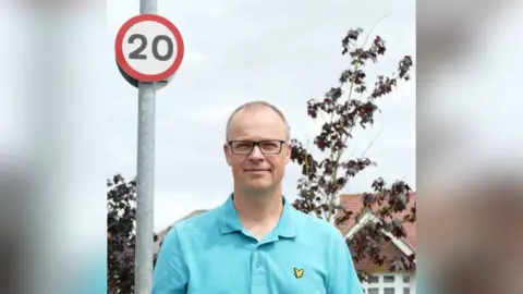 Martin Bailey  Martin Bailey standing in front of a 20mph sign