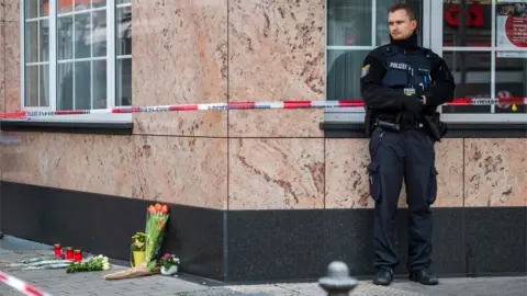 Getty Images A policeman stands next to some flowers left at the scene of the shooting in Hanau