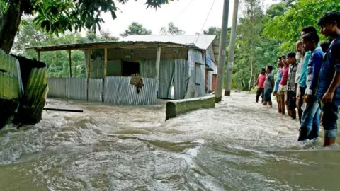 AFP Bystanders watch floodwaters rage near a house in Kurigram, northern Bangladesh.