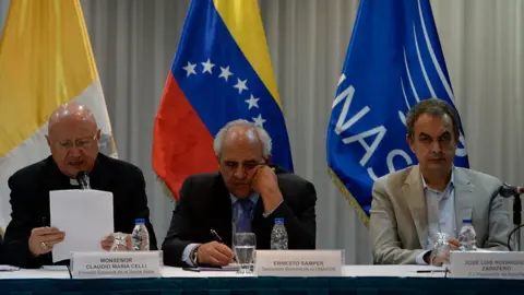 Getty Images The Vatican's pontifical council for social communications, Monsignor Claudio Maria Celli, UNASUR General Secretary Ernesto Samper and former President of the Spanish government Jose Luis Rodriguez Zapatero are seen during a meeting between Venezuela's government and opposition leaders for Vatican-backed talks, in a bid to settle the country's deepening political crisis