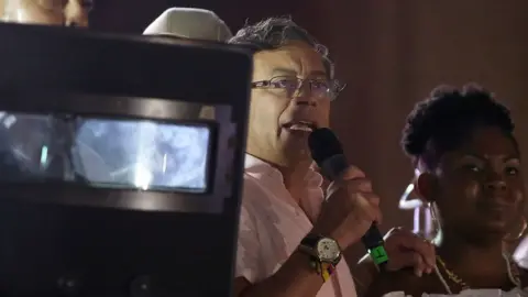 Getty Images Colombian presidential candidate left-wing Gustavo Petro, accompanied by his Vice presidential formula Francia Marquez, delivers a speech covered by a bodyguard holding a bulletproof shield during a campaign rally in Cali, Colombia, May 19, 2022.