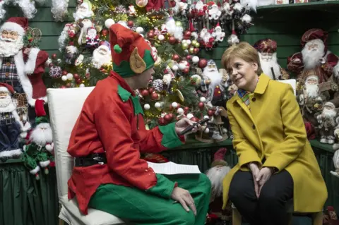 Jane Barlow / PA Media Nicola Sturgeon is interviewed by a journalist dressed as a Christmas elf