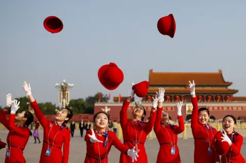 Thomas Peter/ Reuters Ushers dressed in red throw their hats in the air.