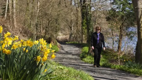 PA Media A Woman Walks Alone Down A Trail Along The Water