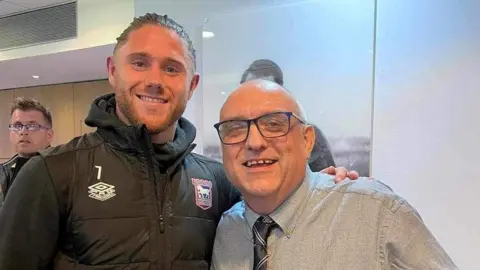 Steve Kirby Gary Battle in a shirt and tie, having his picture taken with Ipswich Town's Wes Burns at the club's training ground