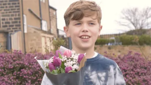 Ewan standing and smiling with bunch of flowers