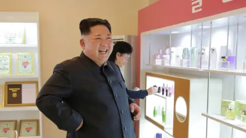 KCNA via Reuters Kim Jong Un smiles near a pink-branded selection of cosmetics