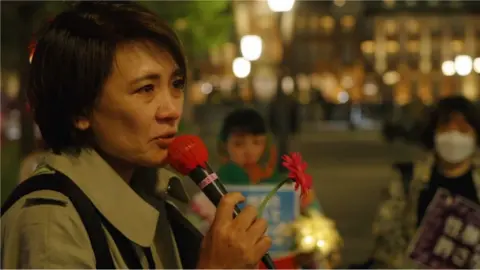 Minori Kitahara holding a microphone and a flower at the Flower Demo in Tokyo