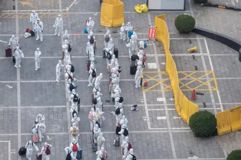 Getty Images Residents wearing personal protective equipment (PPE) line up to enter a specialized hotel for medical observation and quarantine as Zhengzhou eases COVID-19 restrictions on November 1, 2022 in Zhengzhou, Henan Province of China.