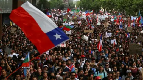 Reuters Demonstrators march with flags and signs during a protest against Chile"s state economic model in Santiago, Chile October 25, 2019