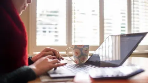 PA Media A woman typing on her laptop