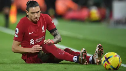 Liverpool striker Darwin Nunez looks at the ball while sitting on the floor