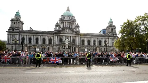 PA Media A crowd of people gathered outside Belfast City Hall to watch the King and Camilla to pass by on their way to St Anne's Cathedral