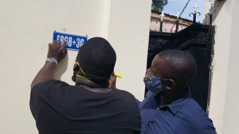 Ade Daramy Bakary Suso (L) and Alieu Sowe, (R) putting a plus code sign on a house in The Gambia