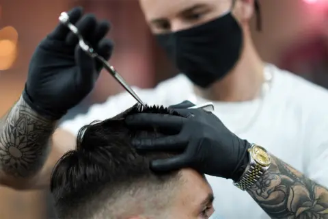 Getty Images A man cuts the hair of another man